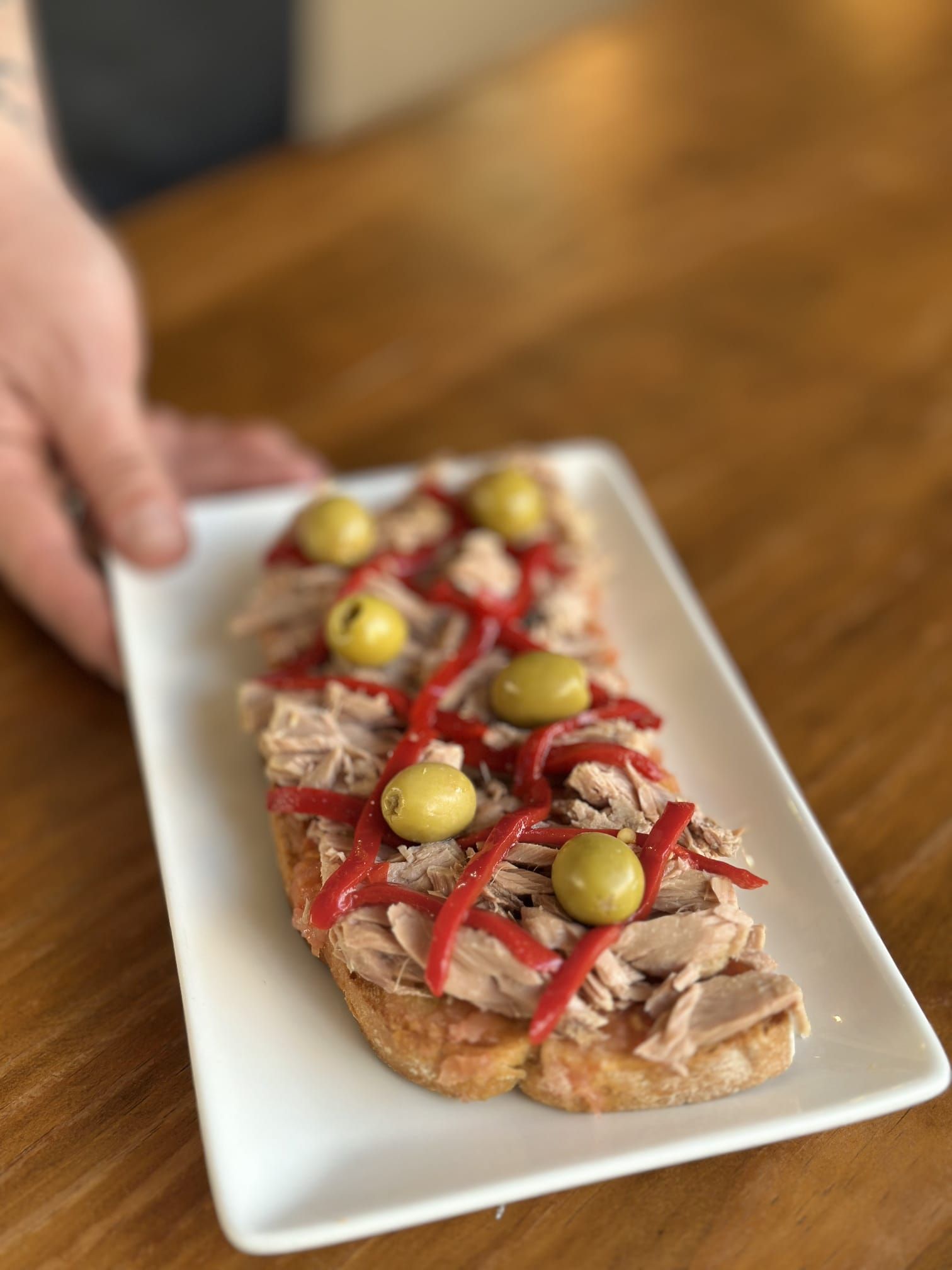 La mano de una persona levanta una porción de pizza con queso sobre un plato, con papas fritas en primer plano.